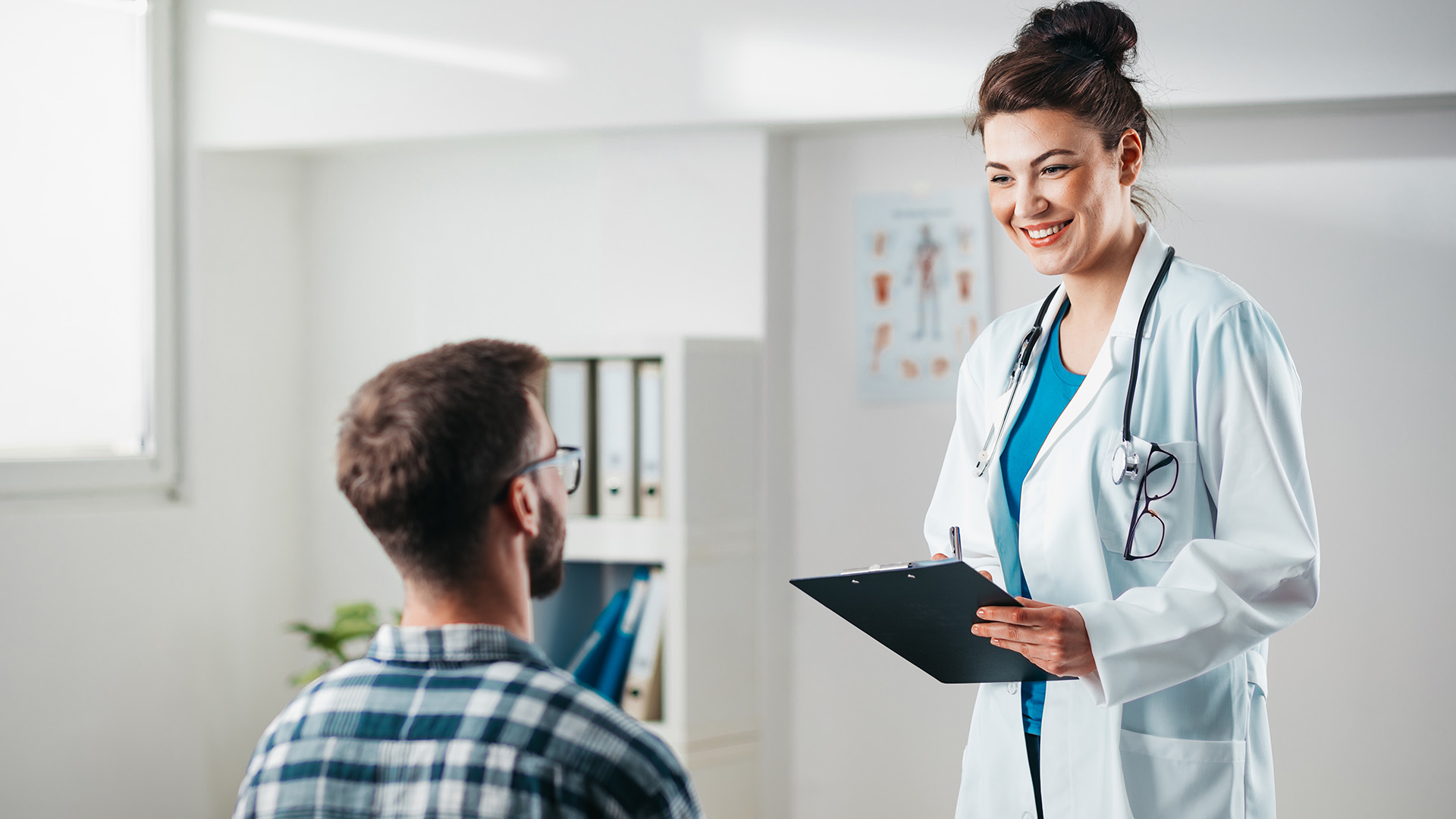 A very tall female doctor with a tiny male patient