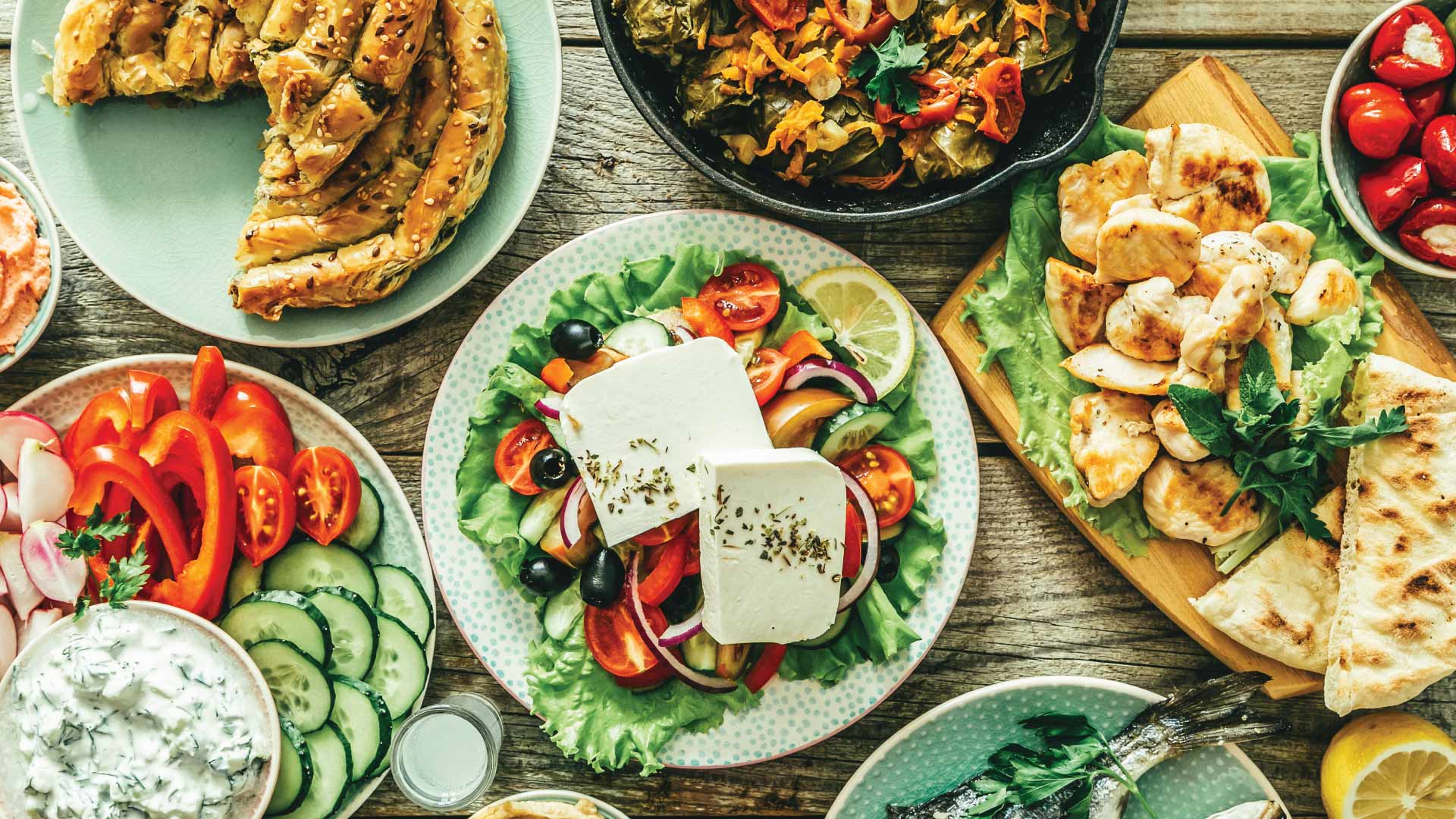 Selection of traditional greek food - salad, meze, pie, fish, tzatziki, dolma on wood background, top view