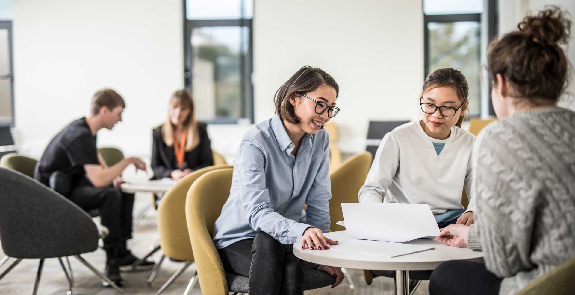 A small group of students sat a a table, with another group sat in the background.