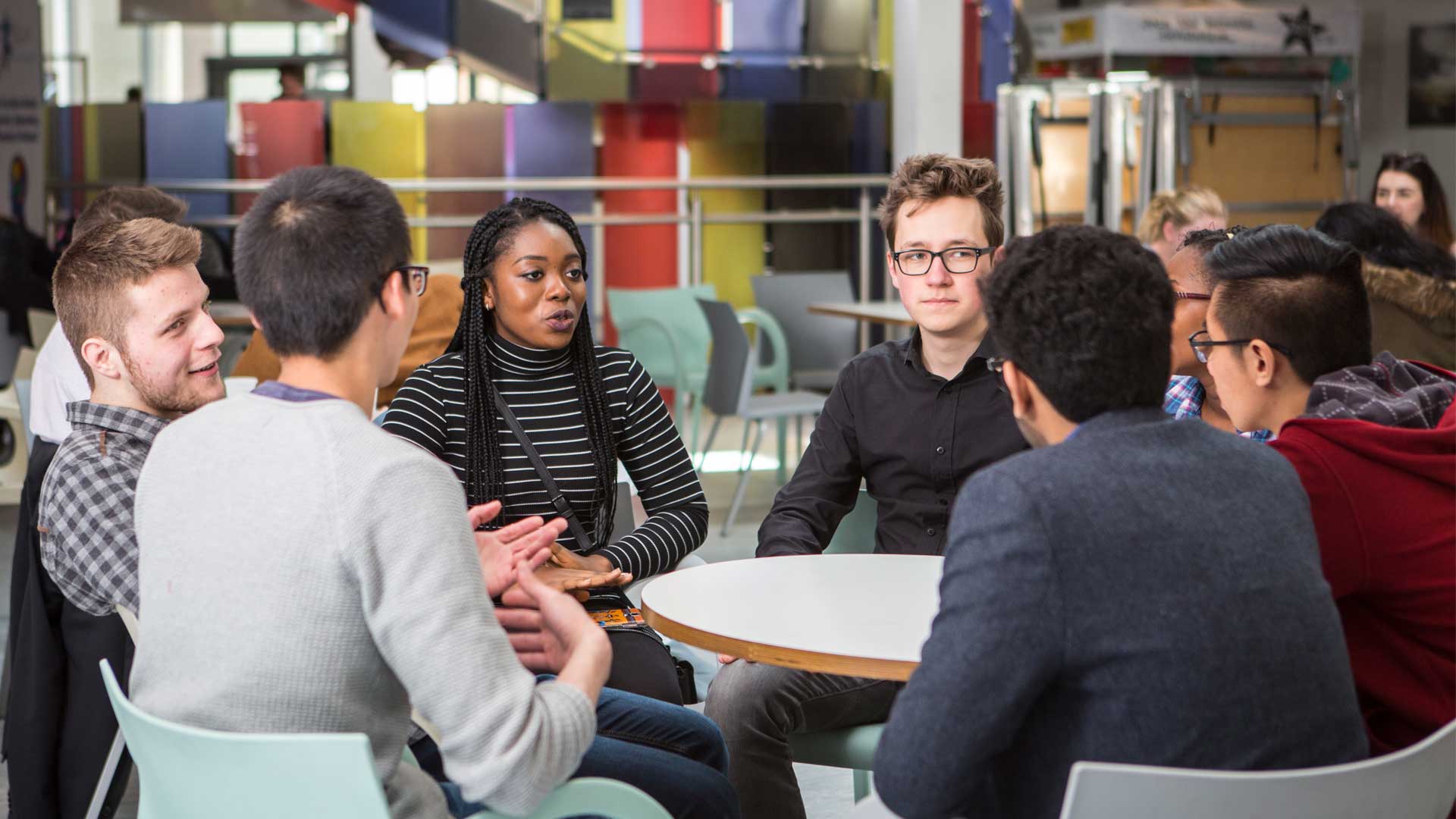 Picture of a group of 8 students chatting in Student Central. Sat around a table.