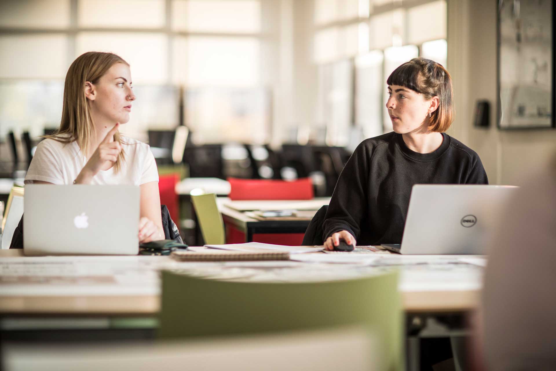 Two interior design students having a discussion whilst working on their laptops